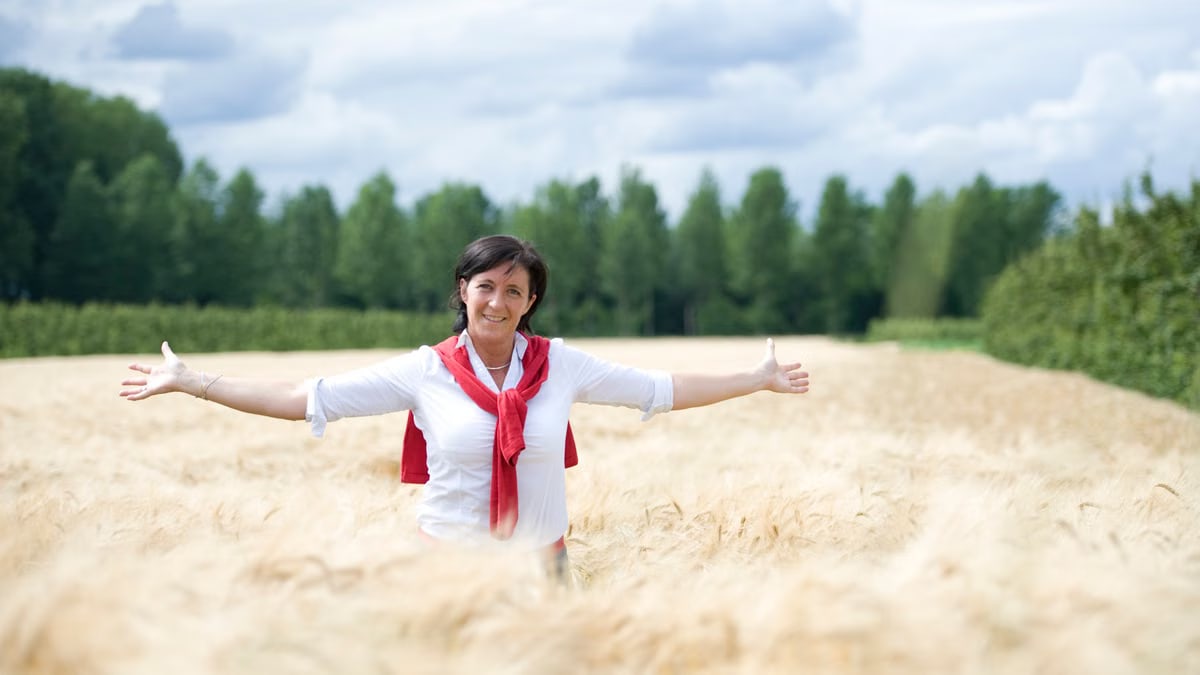 A cheerful woman stands in a wheat field with arms spread, embodying freedom and joy.